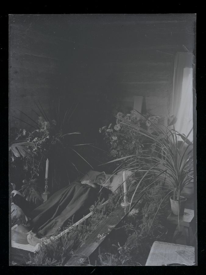 Matusefoto, vana naine avatud kirstus, kirst ümbritsetud lillede ja okstega.