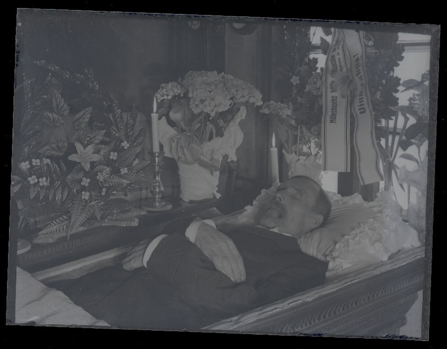 Matusefoto, vana mees lahtises kirstus, kirstu ümber lilled.