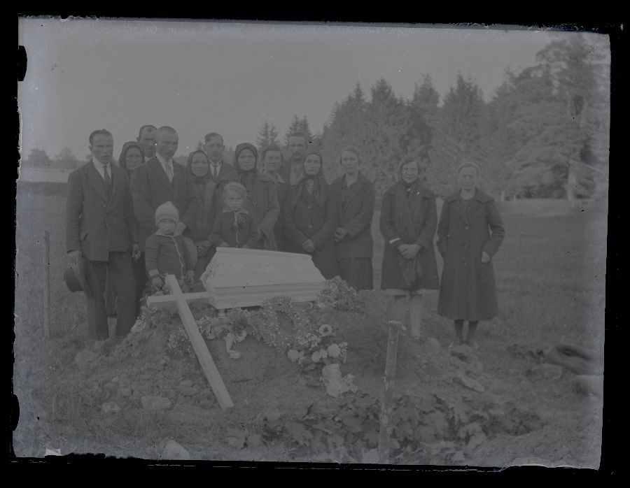 Matusefoto, lapse matus, suletud kirst haua kõrval, kirstu taga seisavad matuselised.