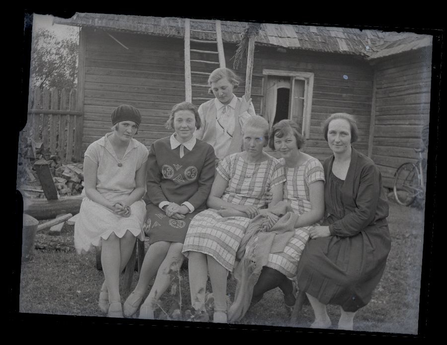 Grupifoto, kuus naist istuvad pingil, taustal maja.