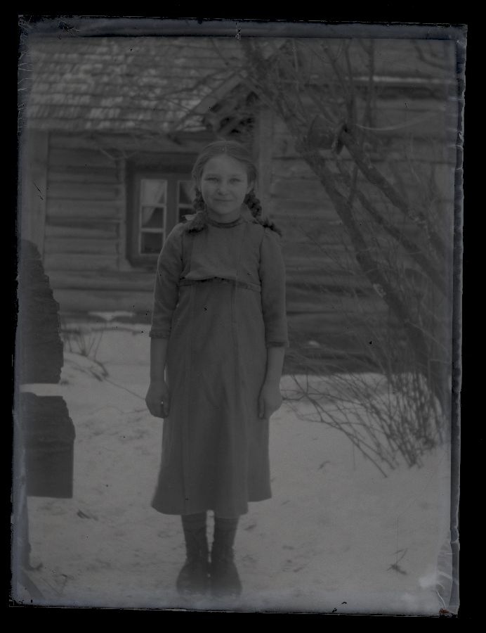 Väike tüdruk, pildistatud talvel taluhoovis, taustal talumaja sein.