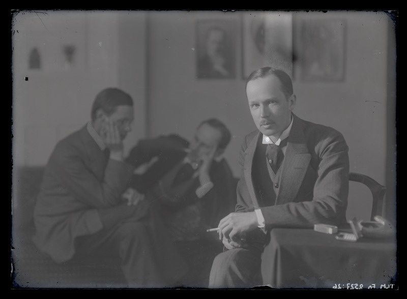 Johannes Parikase portreefoto, ateljee tagapõhjal kaks istuvat meesfiguuri, umbes 1915. aastast.