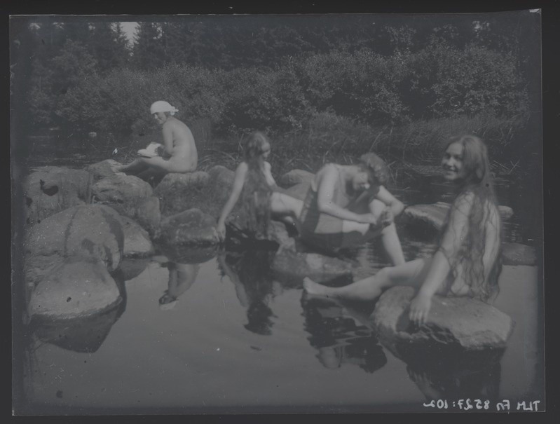 Grupifoto, neli naisfiguuri veekogu kaldal kividel istumas, umbes 1915. aastast.