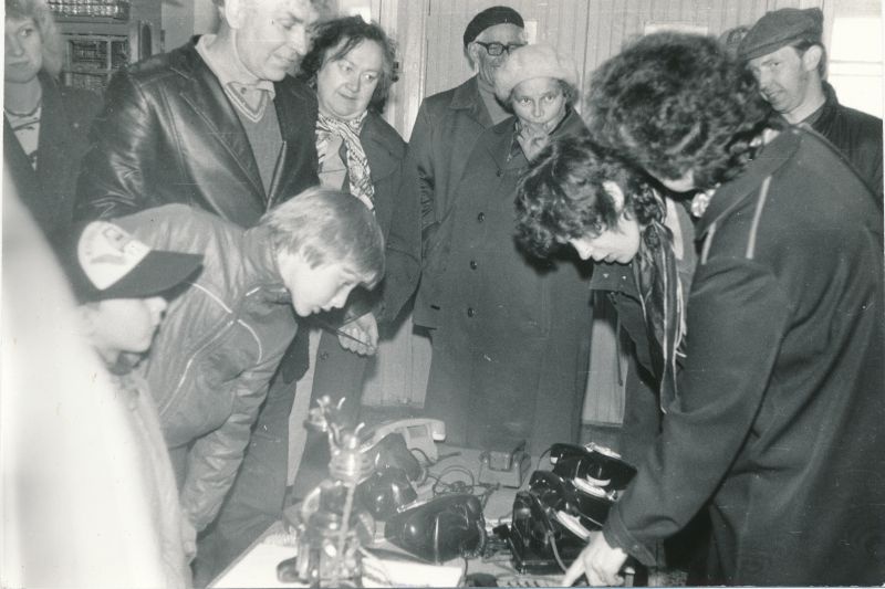 Foto. Karuse Sidemuuseumi  telefoni kollektsiooni väljapanek 1987. Sidesõlme töötajad tutvuvad väljapanekuga.