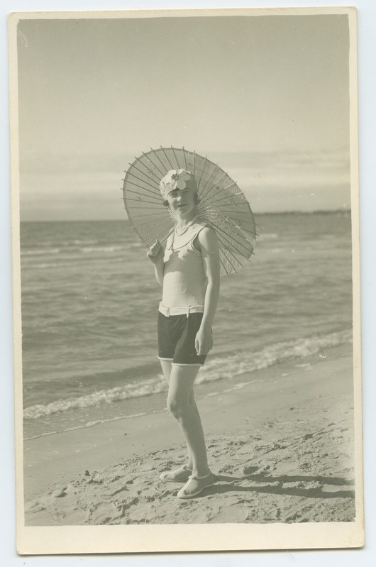 Merepiiril, rannaliival, noor, trikoos, päikesevarjuga naine.