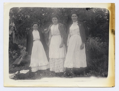 Väljasõit rohelusse. Metsa all kolm teenijannat, õlgadel jakid, ees valged, satsidega põlled.  duplicate photo