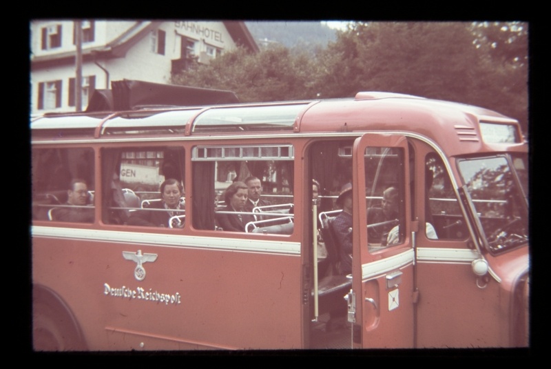 Red bus with the symbol "Deutsche Reichspost", through the glass to see insiders. Over the roof of the bus, the wall of the building with the record "Bahnhotel".