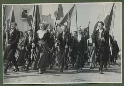 XII üldlaulupidu 28.-29. juunil 1947, Tallinnas.
12. üldlaulupeo rongkäigulised jõudmas Tallinna laululavale. Erinevaid lippe kandvad rahvariietes laulupeolised rongkäigus. Ühel lipul paistmas sirbi ja vasara kujutis. Tagaplaanil paistab Tallinna vana laululava, mille rõdul inimesed rongkäiku jälgivad.  duplicate photo