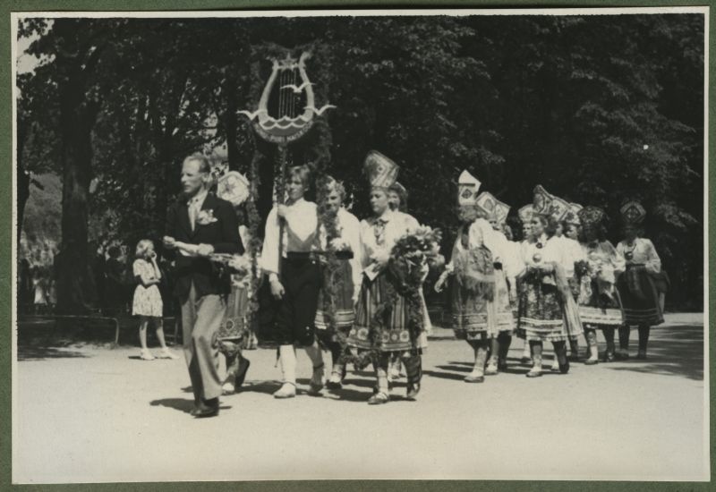 XII üldlaulupidu 28.-29. juunil 1947, Tallinnas.
Muhu-Piiri naiskoor 12. üldlaulupeo rongkäigul. Rahvariietes naised kannavad Muhu-Piiri naiskoori silti, ees kõnnib meesterahvas, tõenäoliselt koorijuht.