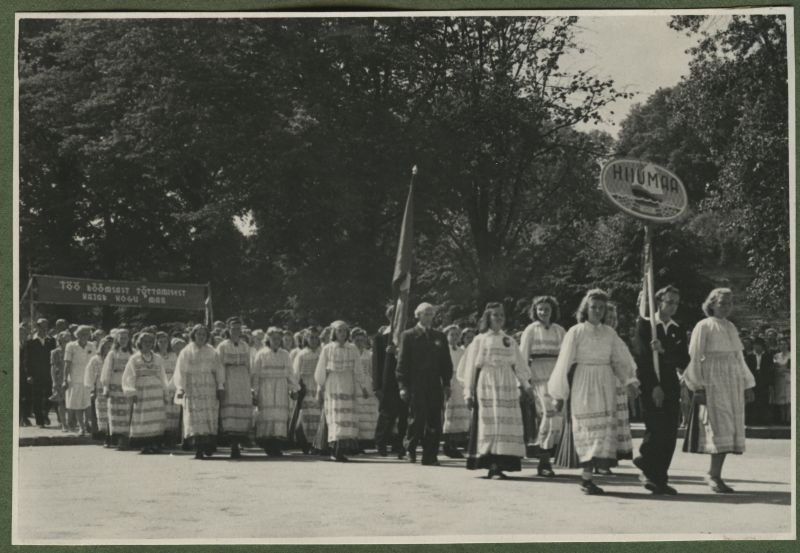 XII üldlaulupidu 28.-29. juunil 1947, Tallinnas.
Hiiumaa esindajad 12. üldlaulupeo rongkäigul. Rahvariietes hiidlased esireas kannavad Hiiumaa silti, neist tagapool kantakse lippu. Rongkäigu tagumises osas kantakse loosungit: "Töö rõõmsast tõttamisest kajab kogu maa".