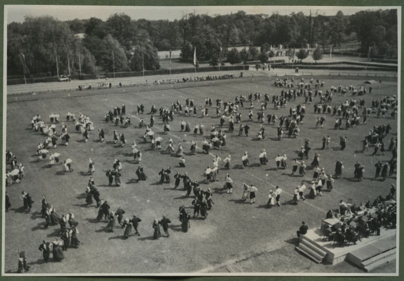 XII üldlaulupidu 28.-29. juunil 1947, Tallinnas.
Rahvariietes tantsijad rahvakunstiõhtul 12. üldlaulupeo eelõhtul Kadrioru staadionil.
Segapaaridest koosnevad rahvatantsurühmad, kes on riietatud erinevatesse rahvariietesse tantsivad sõõris. Tegemist võib olla kaera-jaani tantsimisega. Fotol on näha vähemalt 15 erinevat rahvatantsurühma.