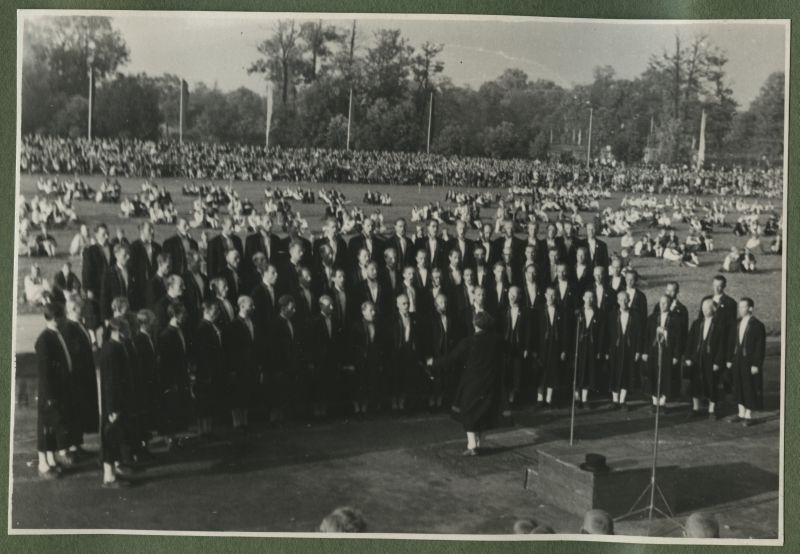 XII üldlaulupidu 28.-29. juunil 1947, Tallinnas.

Meeskoor esinemas rahvakunstiõhtul 12. üldlaulupeo eelõhtul Kadrioru staadionil. Koori ees dirigeerib pidulikult riietatud meessoost koorijuht.
Tagaplaanil maas istumas rahvatantsijad.