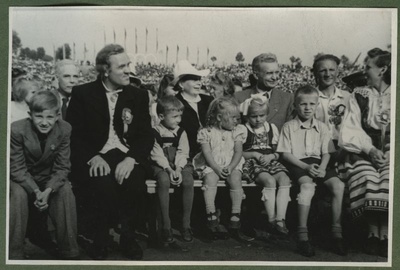 XII üldlaulupidu 28.-29. juunil 1947, Tallinnas.
Pealtvaatajad 12. üldlaulupeol Tallinna lauluväljakul. Pingil istuvad viist last ja rahvariietes paar. Taustal paistavad teisedki pealtvaatajad.  duplicate photo