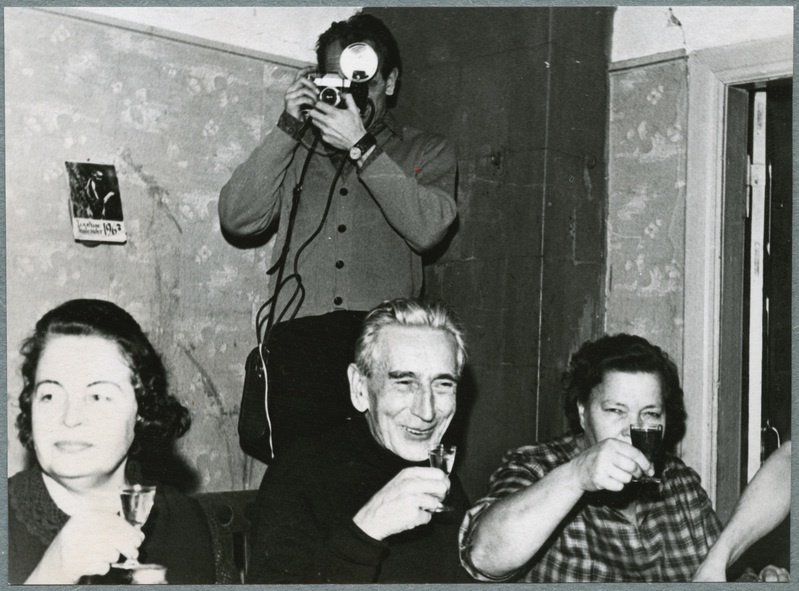 Joann Ümariku sugulased ja tuttavad. Kaks naist ja mees peolaua ääres pitsi tõstmas,  taga nurgas mees fotokaameraga..