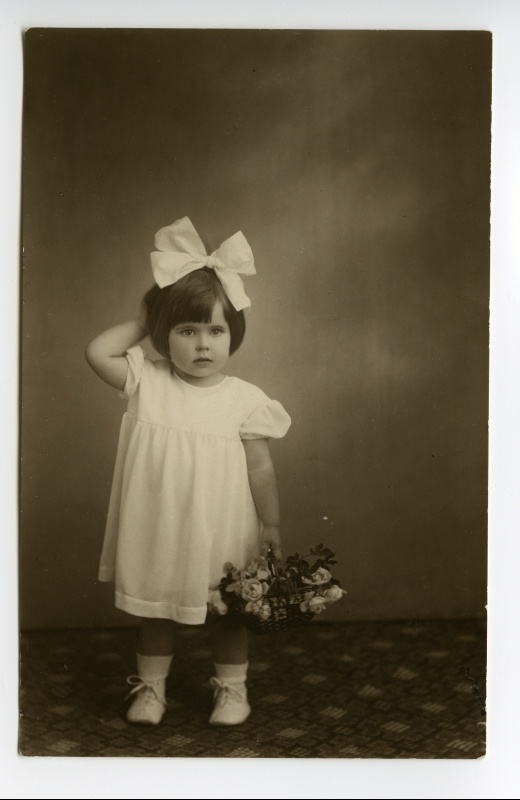 Umbes kahe-aastane tüdrukuke valges kleidis suure valge tutiga ja  lillekorviga.