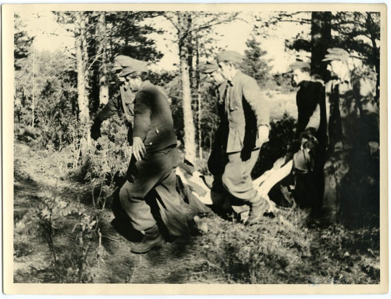 Saksa fašistide roimajäljed 1944.a. Saksa sõjavangid laipa kandmas. Esiplaanil kuus sõjavangi laipa kandmas, tagaplaanil mets.