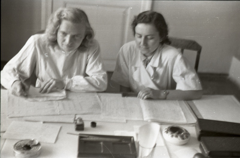 Kaks naist kitlites kirjutuslaua taga istumas