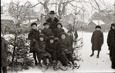 Seitse poissi kahe kuuse vahel seismas ja istumas tõukekelkudel, mees nende seljataga seismas (Poeglastekooli õpilased Tartu Peetri kiriku juures asuval liuväljal)  similar photo