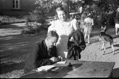 Ilutrüki trükikoja juhataja Leonhard Kahl (vasakul) õues laua taga istumas ja naine heledas kleidis tema juures seimas  similar photo