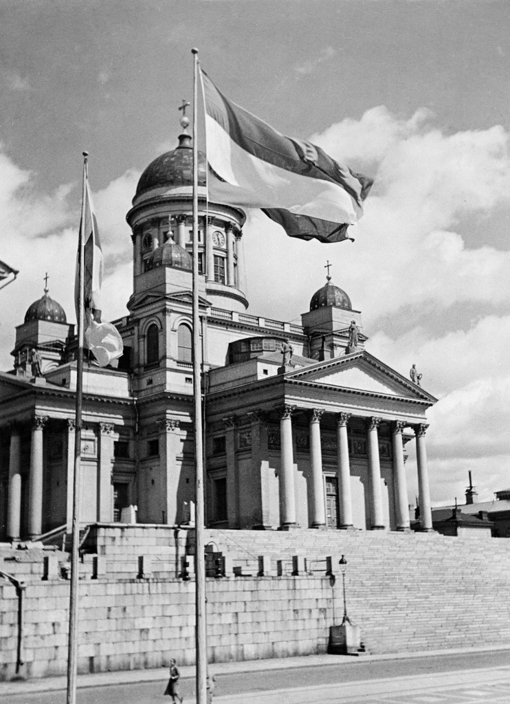 Helsingin Tuomiokirkko (Nikolainkirkko, Suurkirkko) yliopiston päärakennuksen portailta. Liput Suomen, Unkarin ja Viron.