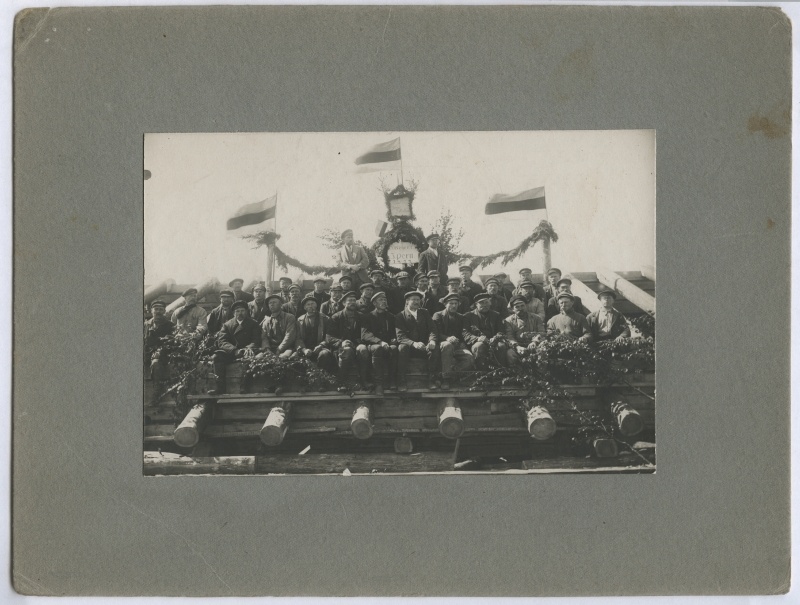 Grupipilt: ehitajad sarikapeol. Pärgade ja lippude vahel tahvel kirjega "Inseneer J. Pern 1922".