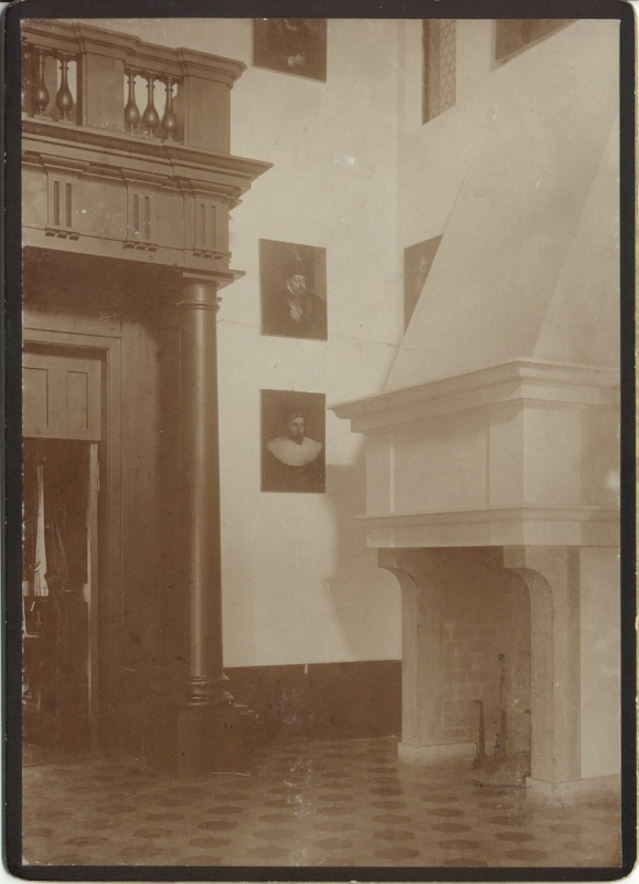 Alatskivi. The hall of the manor. On the left the dark door leads to indoors. On the right high white fireplace; on the white wall crocheted portraits of the manor owner's ancestors.
