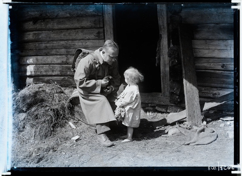 Seljakotiga mees (matkaja) majauksel lapsega vestlemas, mehel süles väike koer.