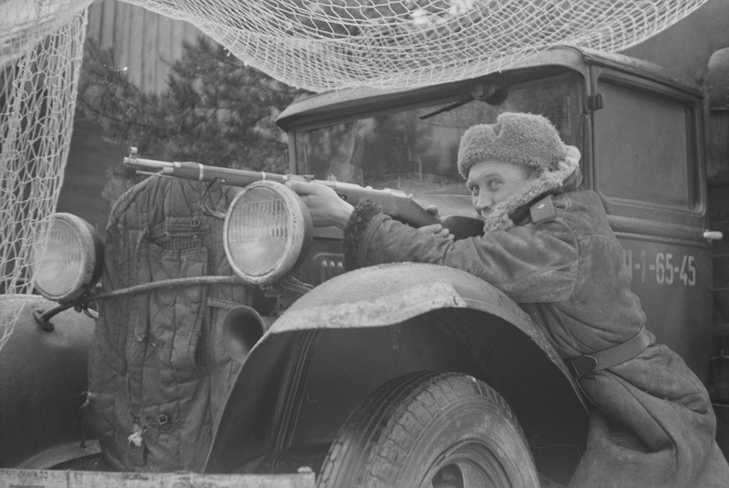 Sõdur relvaga laskepoosis sõjaväeauto najal poseerimas