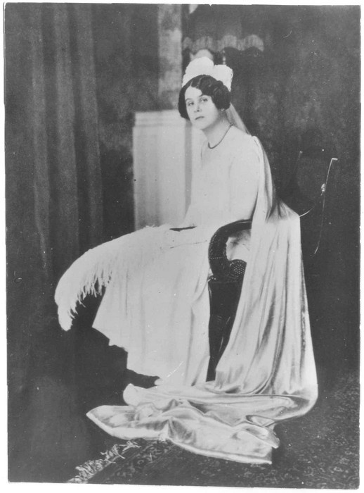 Portreefoto. Aino Kallas heledas kleidis, käes sulg