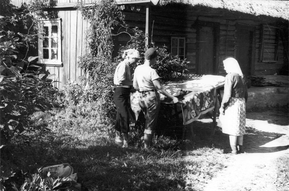 Muuseumitöötajad ja Elena Ristnok (paremal) Mihkli talu õuel roositud tekki vaatamas.