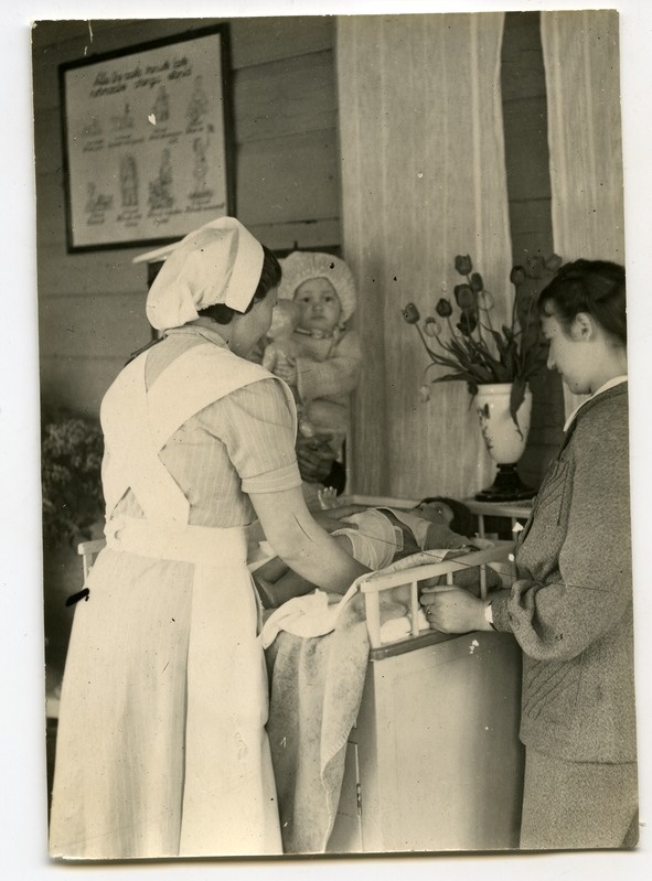 Kuressaare lastesõim: kasvataja näitab emale nuku peal imiku mähkimist