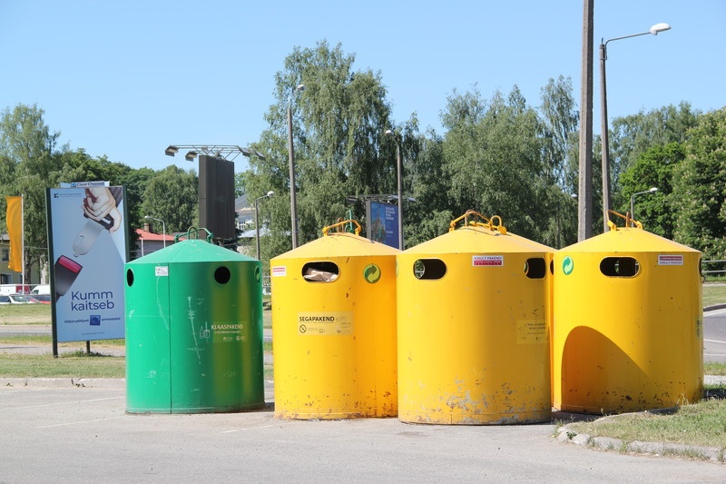 Digifoto. Jäätmete kogumise konteinerid Rebase Rimi hüpermarketi juures, vasakul liiklusreklaam. Tartu, 2018.