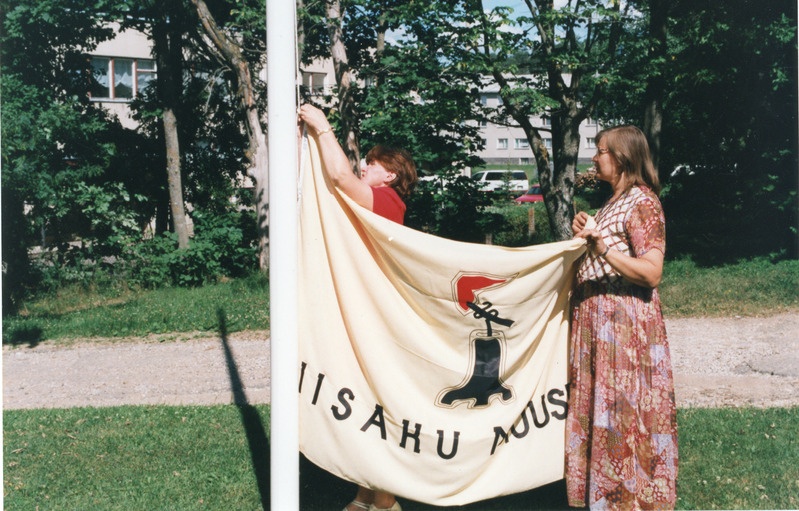 Iisaku muuseumi logoga lipp. Lipu juures Ülle Marits, Kaja Tina