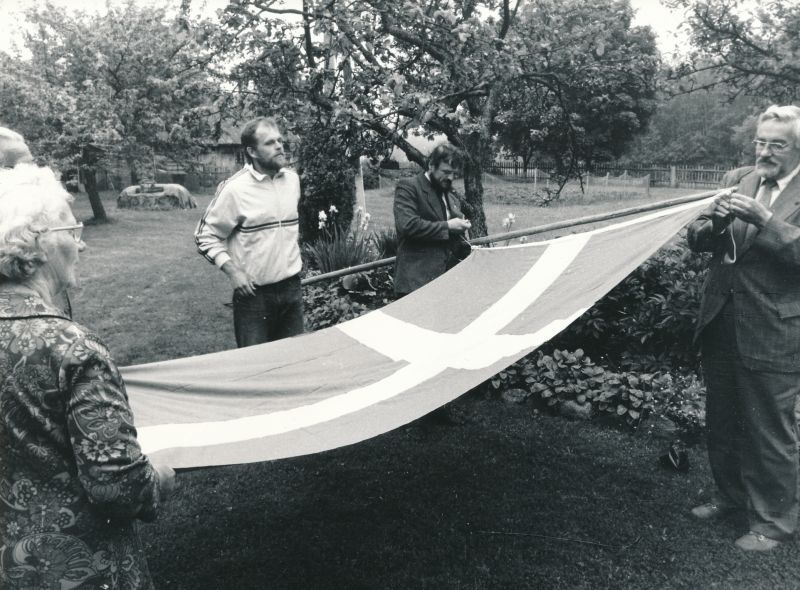 Foto. Rootsi Kuningriigi peakonsuli Leningradis hr. Bengt Akerreni Vormsil 21.juunil 1988.a.
Fotol vasakult Vormsi abimetsaülem Ants Varblane, Eestirootslaste Kultuuriseltsi esimees Ain Sarv ja seltsi aseesimees Maido Limbak konsuli poolt kingitud Rootsi lipuga. 
Foto: Arvo Tarmula.