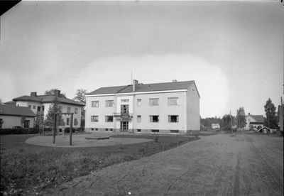 Rapattu kaksikerroksinen "Opettajien talo" (kauppalan opettajille rakennuttamia työsuhdeasuntoja) syyskuussa 1956. Eerontien puoleinen julkisivu. Tämän vieressä Ester Bäckmanin rakennuttama huvila, jossa toimi kuvaushetkellä Käsineteollisuus Oy. Pihalla kaksi pientä lasta keinumassa.
Kuva: Väinö Kermisen kokoelma/Keravan museopalvelut  duplicate photo
