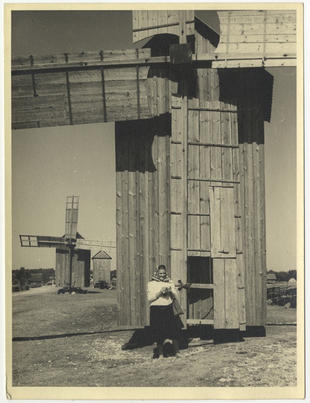 Vormsi rahvariietes naine kott käes seismas pukktuuliku tiibade juures.