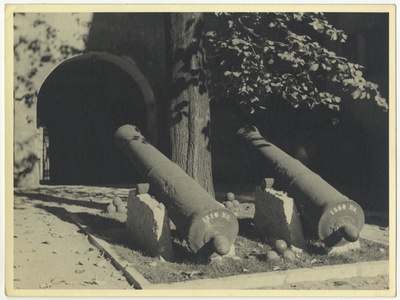 Kaks vanaaegset eestlaetavat kahuritoru puu all võlviga kangialuse ees.  duplicate photo
