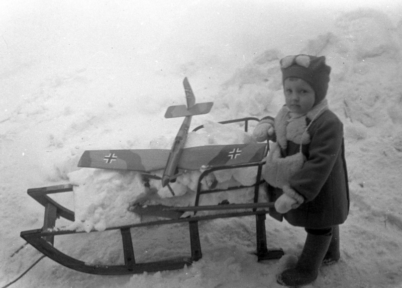 Väike laps kelguga, kelgul lumi ja lennuk, käes labidavars