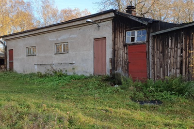 Paloaseman palokalustovaja Vallisaaressa. Siinä säilytettiin aikanaan T-mallista Fordia, kuorma-autoa ja hevosvetoisia kärryjä. Keskimmäisestä ovesta kuljettiin kahden hevosen talliin ja viereisestä punaisesta ovesta hevosten rehu- ja heinävarastoon. Pihapiiriin kuuluu myös vasemmassa reunassa näkyvä puusepänverstas. Valokuva on otettu aurinkoisella säällä. rephoto