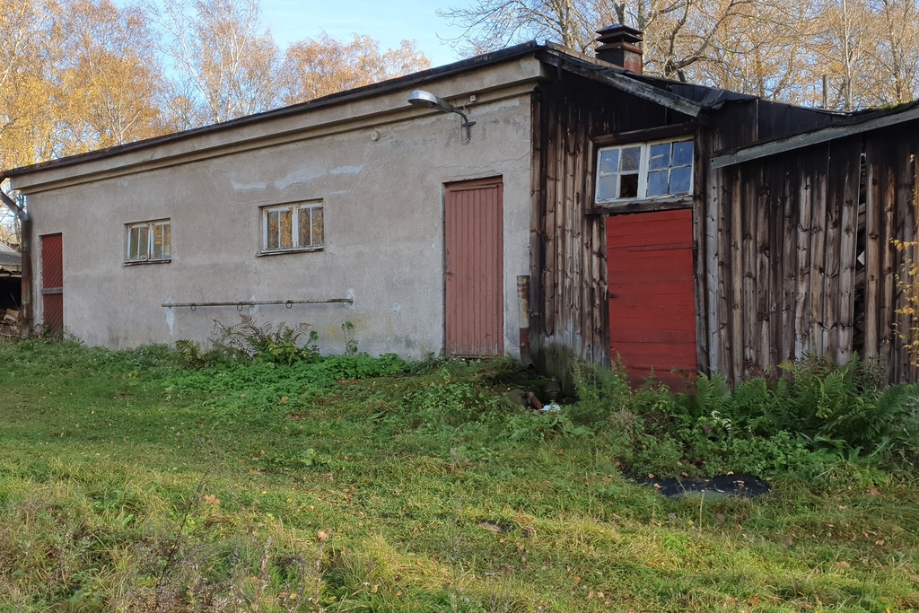 Paloaseman palokalustovaja Vallisaaressa. Siinä säilytettiin aikanaan T-mallista Fordia, kuorma-autoa ja hevosvetoisia kärryjä. Keskimmäisestä ovesta kuljettiin kahden hevosen talliin ja viereisestä punaisesta ovesta hevosten rehu- ja heinävarastoon. Pihapiiriin kuuluu myös vasemmassa reunassa näkyvä puusepänverstas. Valokuva on otettu aurinkoisella säällä. rephoto