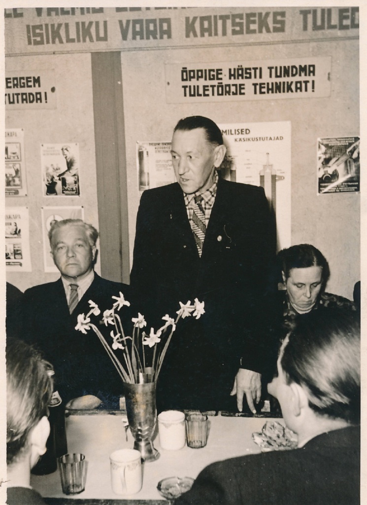 Grupifoto. Pidulik koosviibimine Tartu tuletõrjedepoos. Vasakult esimene Eduard Türn. Tagaseinal tuletõrje-alased loosungid. Tartu, 1970-1980ndatel.
