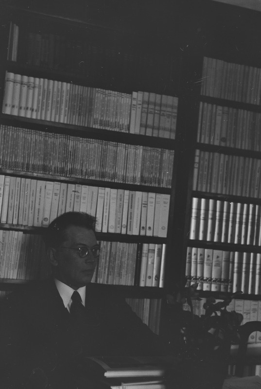 Friedebert Tuglas istumas raamaturiiuli taustal