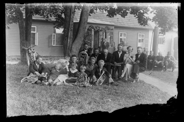 Company with celebratory clothes and musical instruments in front of the house on the lawn