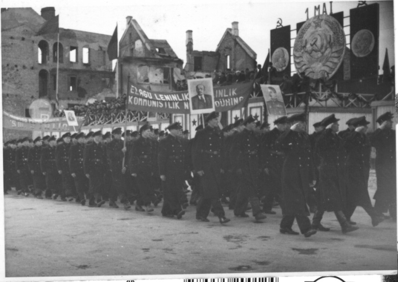 Employees' train trip in Tartu: at the market building; with broken buildings on the street.