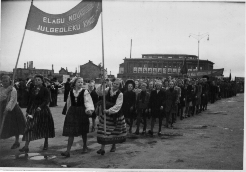 Employees' train trip in Tartu: at the market building; with broken buildings on the street.
