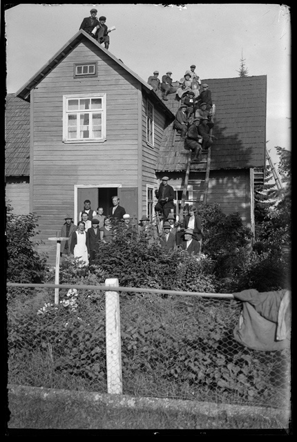 Company of men and women in front of the house and on the roof in 1937