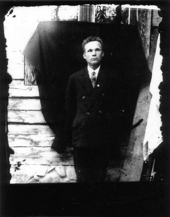 Klaasnegatiiv. Mees maja seina ees, taustaks mantel
