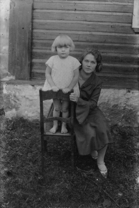 Klaasnegatiiv. Maja ees tooli seisab väike tüdruk, tema kõrval istub naine (Muda kooli õpetaja)