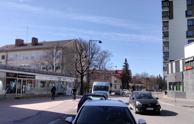 Katunäkymä Aleksis Kiven tien varrelta 1950-luvun jälkipuoliskolta. Vasemmalla vuonna 1957 valmistuneen Suomen Työväen Säästöpankin (STS) matala liikesiipi, jonka takana Keravan kauppalantalo. Kauppalantalon päädyssä Keravan ensimmäinen kuntavaakuna. Kauppalantalon takana näkyy vuonna 1952 valmistuneet kauppalan virkailijoiden lamellitalo (ns. haitaritalo). Tien oikealla puolen maalarimestari Blommin talon kulmaa, jossa kuvaushetkellä toimi Kelloliike T.Soikkeli.  Päällystämättömällä tiellä pyöräilee pariskunta.
https://muistaja.finna.fi/keravan_museopalvelut/Record/kerava_mui.mui-15460 rephoto