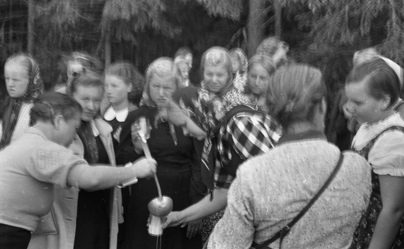 Naine kulbiga neiudele juua klaasi valamas looduses (Väljasõit mootorpaatidega, Tütarlastekool)